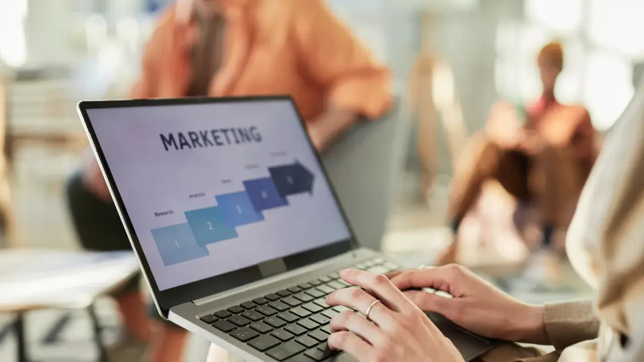 Osoba pracuje na laptopie z prezentacją "MARKETING". Widoczne etapy: Research, Analysis, Sales. Idealne do studiów zarządzanie i marketing.