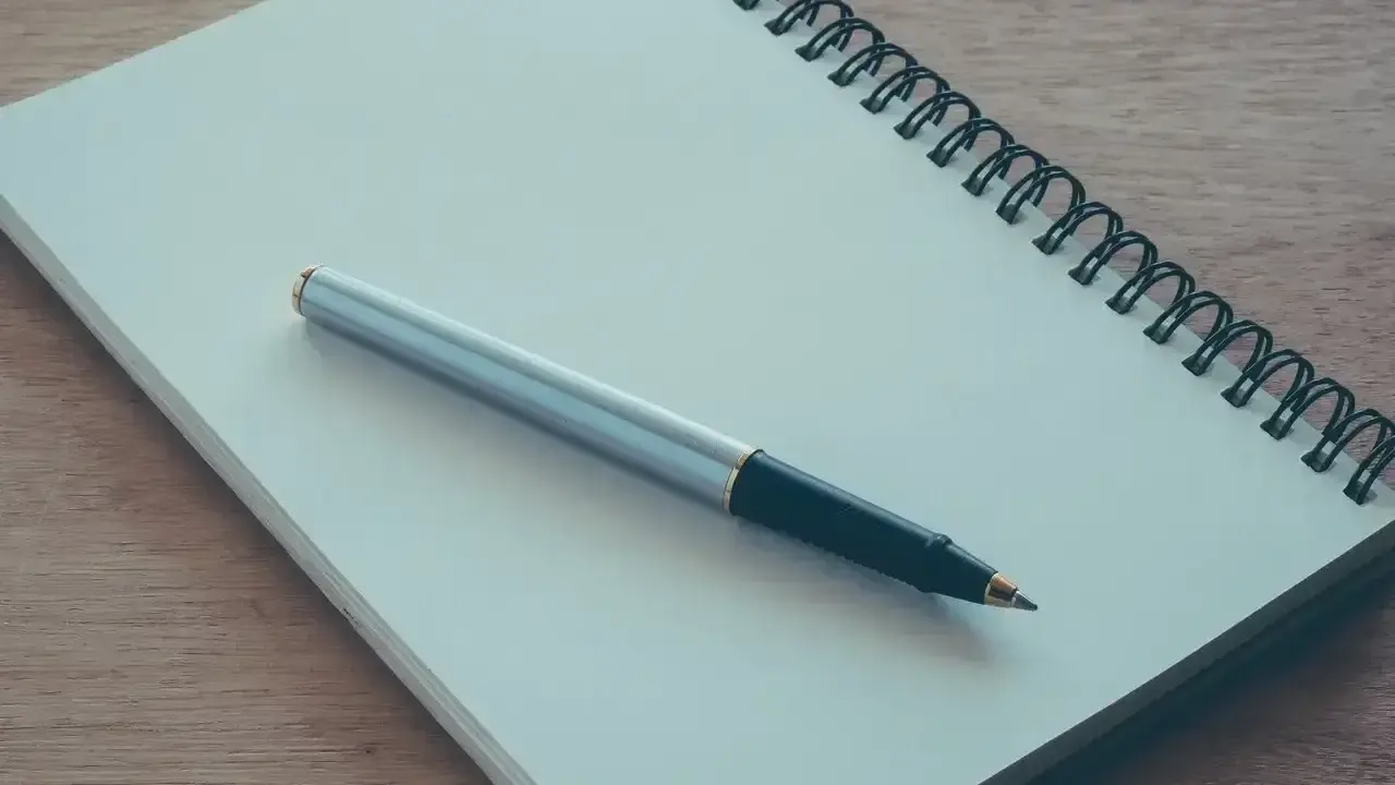 Notes for a podanie o pracę leżą na drewnianym blacie. Długopis czeka na rozpoczęcie pisania.