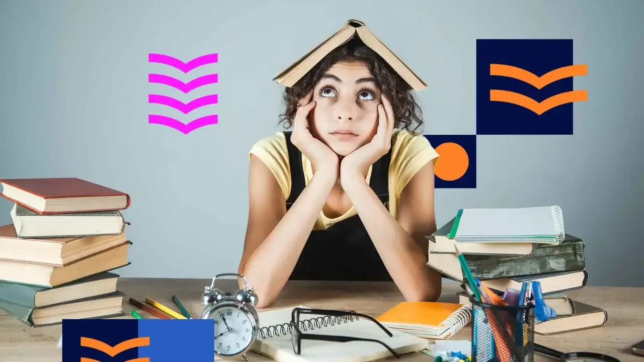 Zmęczona studentka z książką na głowie, otoczona stosami książek i materiałami do nauki. Tak wyglądają studia niestacjonarne.