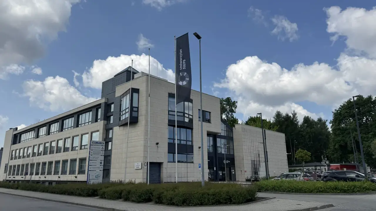 Nowoczesny budynek Uniwersytetu SWPS, jednej z uczelni w Krakowie, z flagą i parkingiem.