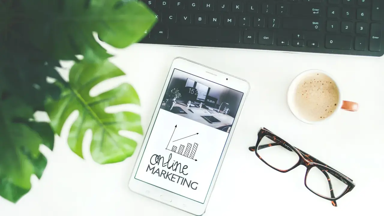 Biurko z tabletem pokazującym wykresy i hasło "online MARKETING", obok klawiatura, kawa i okulary. Idealne do social media studia.