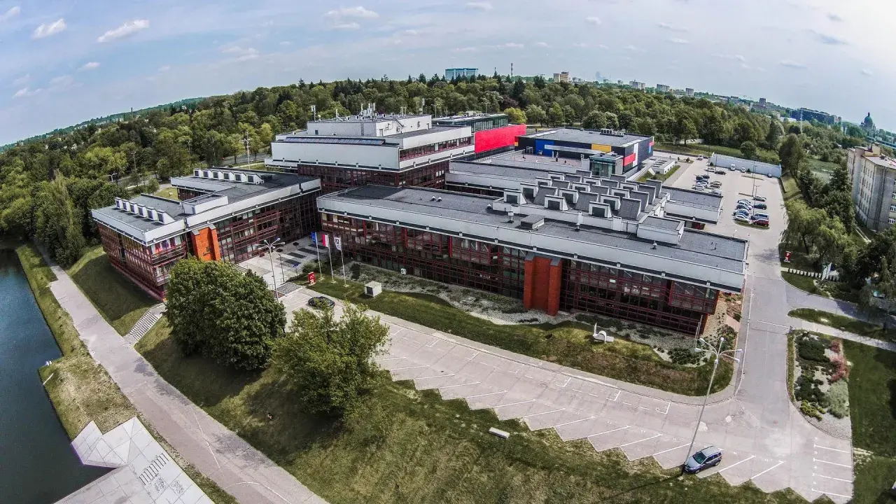 Nowoczesne budynki uczelni w Łodzi, otoczone zielenią, z widokiem na miasto.