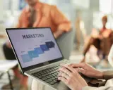 Osoba pracuje na laptopie z prezentacją "MARKETING". Widoczne etapy: Research, Analysis, Sales. Idealne do studiów zarządzanie i marketing.