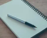 Notes for a podanie o pracę leżą na drewnianym blacie. Długopis czeka na rozpoczęcie pisania.