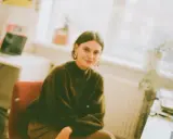 Młoda kobieta w zielonym swetrze siedzi przy biurku, przygotowując się do zajęć z architektura studia zaoczne.
