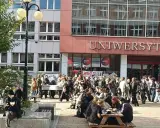 Grupa studentów przed budynkiem z napisem "UNIWERSYTET". Zastanawiasz się, czym się różni akademia od uniwersytetu?