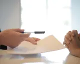 Dłonie trzymają dokumenty i długopis. Przygotowanie do napisania listu motywacyjnego dla referenta biurowego.