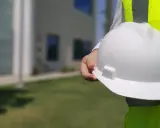 Inspektor BHP trzyma biały kask ochronny na tle budynku.