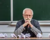 Zamyślony adiunkt, kto to? Siedzi przy biurku, przed nim pogięte kartki.