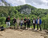 Grupa studentów studiów ochrona środowiska podziwia malowniczy krajobraz z klifem i bujną zielenią.