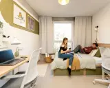 Dwie osoby w pokoju studenckim, jeden leży na łóżku, drugi siedzi obok. Tak wyglądają egzaminy na studiach – chwila wytchnienia przed nauką.