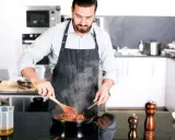 Mężczyzna w fartuchu gotuje na patelni, ucząc się, jak zostać kucharzem.