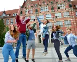 Radosna grupa studentów skacze przed budynkiem, gdzie można podjąć studia psychologiczne Gdańsk.