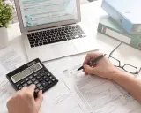 Osoba wypełnia formularz podatkowy, korzystając z kalkulatora i laptopa. To może być początek drogi, jak zostać księgowym.