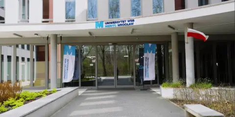 Wejście do Uniwersytetu WSB Merito Wrocław. Flagi z logo uczelni i polska flaga. Idealne miejsce na studia anglistyka Wrocław.