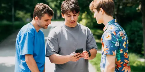Trzech studentów dyskutuje, czy na studiach są wakacje. Jeden z nich pokazuje coś na telefonie.