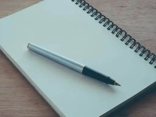 Notes for a podanie o pracę leżą na drewnianym blacie. Długopis czeka na rozpoczęcie pisania.