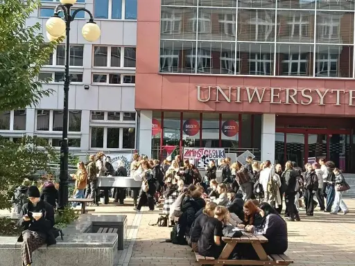 Grupa studentów przed budynkiem z napisem "UNIWERSYTET". Zastanawiasz się, czym się różni akademia od uniwersytetu?