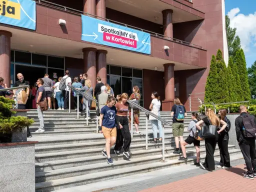 Grupa młodych ludzi schodzi po schodach przed budynkiem, gdzie wisi baner "Spotkajmy się w Kortowie!". To idealne miejsce na rozpoczęcie studiów w Olsztynie.