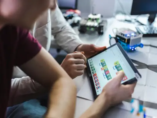 Dzieci programują robota na tablecie, ucząc się, czym zajmuje się informatyk.