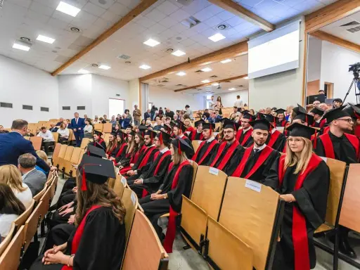 Absolwenci w togach siedzą na uroczystości w sali wykładowej. To ważny dzień dla studentów z Radomia.