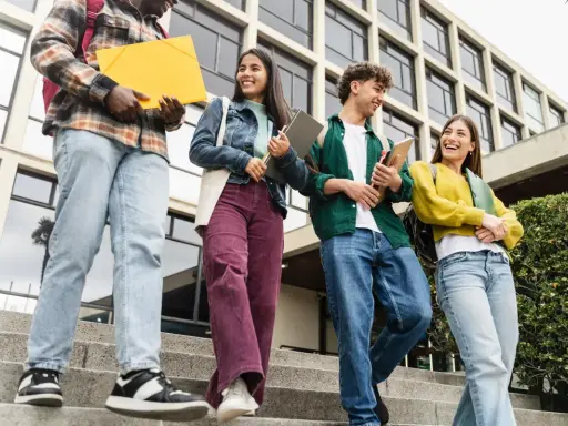 Studenci idą po schodach, rozmawiając i śmiejąc się. Czy ich wysoka średnia pozwoli im zdobyć stypendium?