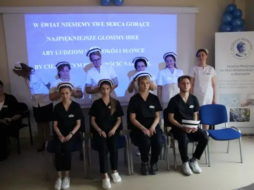 Uczelnia Medyczna im. Marii Skłodowskiej-Curie w Warszawie: studenci w strojach medycznych, z hasłem na ekranie.