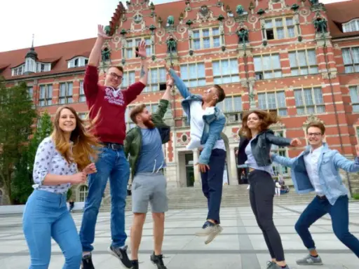 Radosna grupa studentów skacze przed budynkiem, gdzie można podjąć studia psychologiczne Gdańsk.