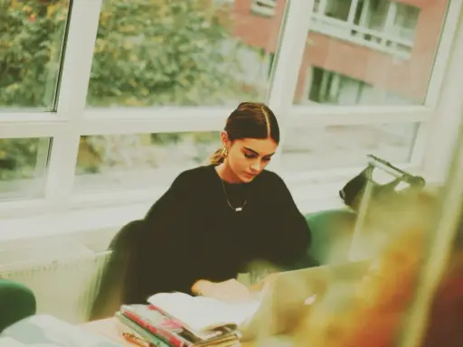 Studentka pochłonięta nauką kryminologii w Poznaniu, siedzi przy oknie z laptopem i książkami.