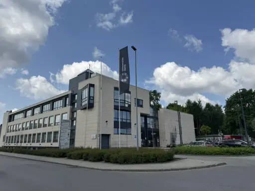 Nowoczesny budynek Uniwersytetu SWPS, jednej z uczelni w Krakowie, z flagą i parkingiem.