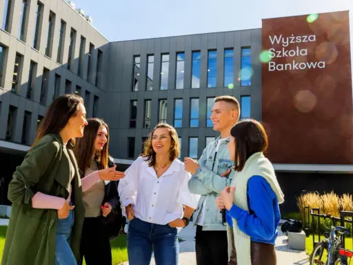 Grupa studentów śmieje się przed budynkiem Wyższej Szkoły Bankowej w Sosnowcu.