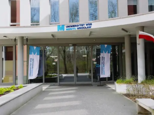 Wejście do Uniwersytetu WSB Merito Wrocław. Flagi z logo uczelni i polska flaga. Idealne miejsce na studia anglistyka Wrocław.