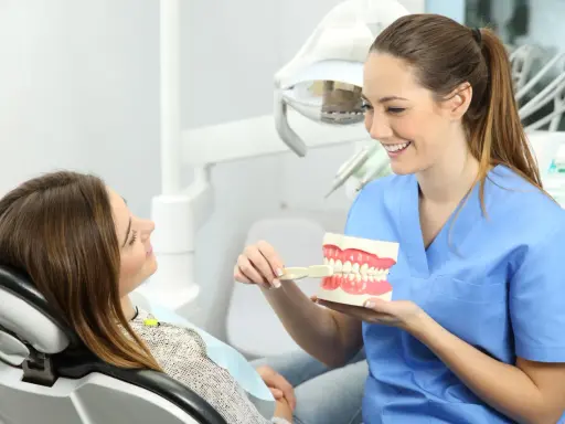 Uśmiechnięta higienistka stomatologiczna pokazuje pacjentce model szczęki. Dobra higena to podstawa, a zarobki higienistki stomatologicznej są satysfakcjonujące.