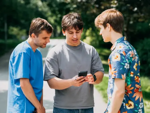 Trzech studentów dyskutuje, czy na studiach są wakacje. Jeden z nich pokazuje coś na telefonie.