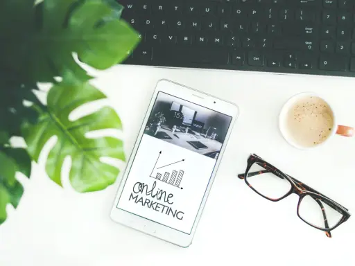 Biurko z tabletem pokazującym wykresy i hasło "online MARKETING", obok klawiatura, kawa i okulary. Idealne do social media studia.