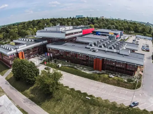 Nowoczesne budynki uczelni w Łodzi, otoczone zielenią, z widokiem na miasto.