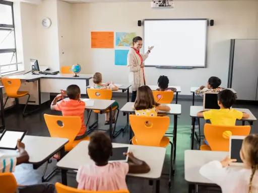 Nauczycielka prowadzi lekcję w klasie pełnej dzieci. To idealne miejsce do nauki pedagogiki przedszkolnej i wczesnoszkolnej w Poznaniu.