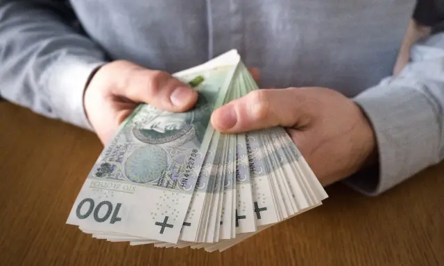 Dłonie trzymające plik banknotów 100 zł. Symbolizuje to zarobki, które mogą być wynikiem najlepiej płatnych zawodów.