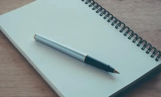 Notes for a podanie o pracę leżą na drewnianym blacie. Długopis czeka na rozpoczęcie pisania.