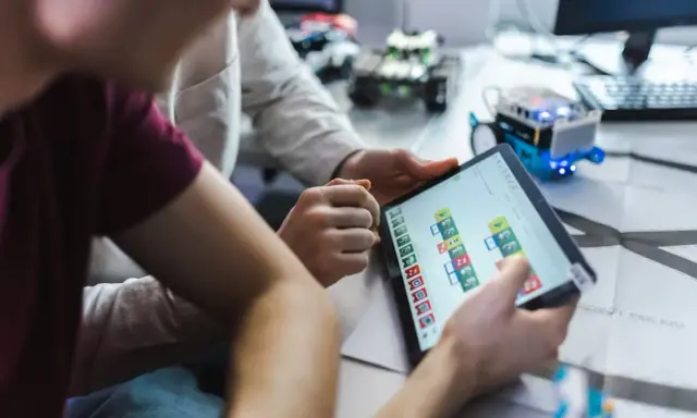Dzieci programują robota na tablecie, ucząc się, czym zajmuje się informatyk.