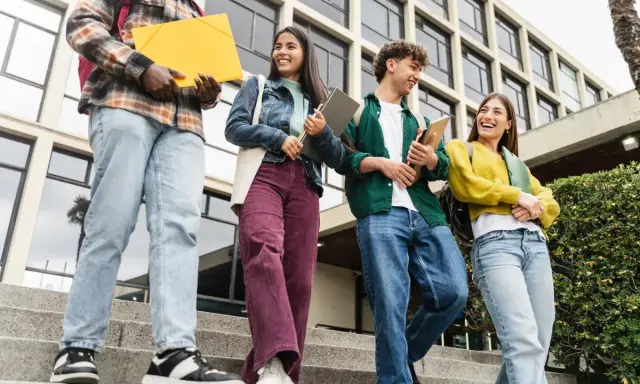 Studenci idą po schodach, rozmawiając i śmiejąc się. Czy ich wysoka średnia pozwoli im zdobyć stypendium?