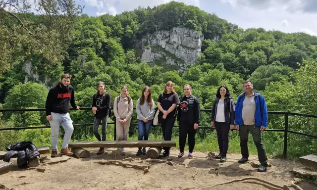 Grupa studentów studiów ochrona środowiska podziwia malowniczy krajobraz z klifem i bujną zielenią.