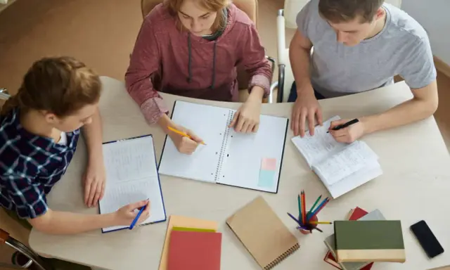 Trzech studentów pracuje nad pracą licencjacką, analizując metody badawcze.