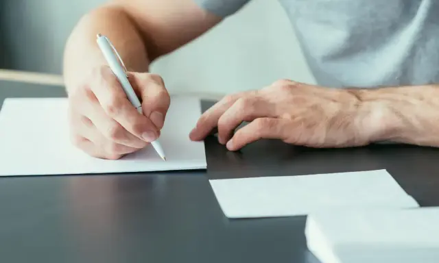 Ręce piszą list motywacyjny specjalista ds sprzedaży. Dokumenty i koperty leżą na biurku.