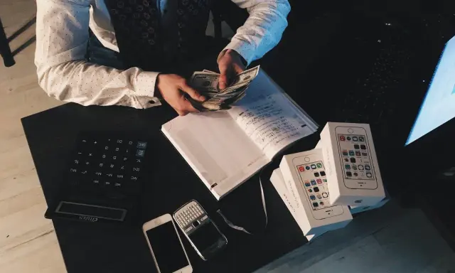 Agent ubezpieczeniowy liczy pieniądze, obok leżą telefony i notatnik. Zastanawiasz się, ile zarabia agent ubezpieczeniowy?