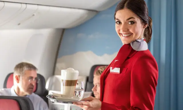 Uśmiechnięta stewardessa w czerwonym mundurku podaje kawę. Czy jej stewardessa zarobki są wysokie?