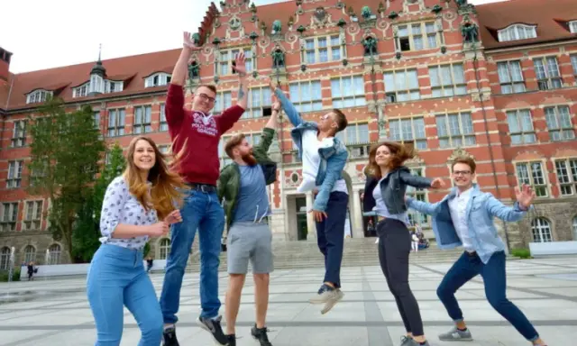 Radosna grupa studentów skacze przed budynkiem, gdzie można podjąć studia psychologiczne Gdańsk.