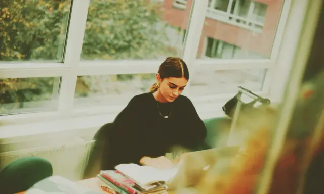 Studentka pochłonięta nauką kryminologii w Poznaniu, siedzi przy oknie z laptopem i książkami.