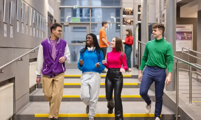Studenci na schodach w nowoczesnym budynku Uniwersytetu Dolnośląskiego.