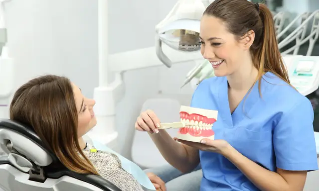 Uśmiechnięta higienistka stomatologiczna pokazuje pacjentce model szczęki. Dobra higena to podstawa, a zarobki higienistki stomatologicznej są satysfakcjonujące.